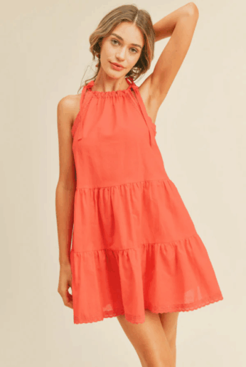 Model wearing short peach dress on cream studio background.